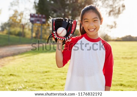 Young Chinese girl holding baseball in mitt looks to camera