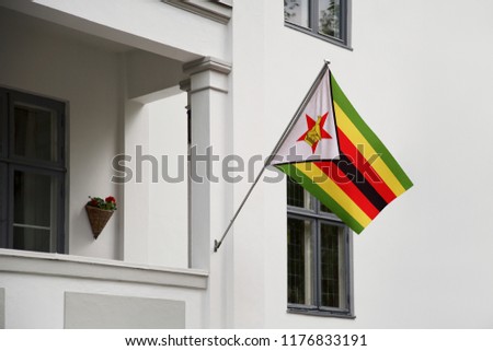 Zimbabwe flag. Zimbabwean flag hanging on a pole in front of the house. National flag waving on a home displaying on a pole on a front door of a building. Flag raised at a full staff.