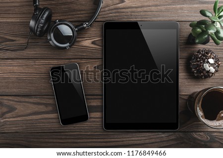 Mock-up blank screen tablet and phone, office desk table with headphones, biscuits and coffee cup. Top view Royalty-Free Stock Photo #1176849466