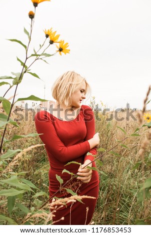 Picture of gorgeous young woman standing in the field. Romantic blonde woman walking in amazing field. Red dress. 