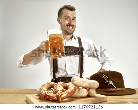 Germany, Bavaria, Upper Bavaria. The young happy smiling man with beer dressed in traditional Austrian or Bavarian costume holding mug of beer at pub or studio. The celebration, oktoberfest, festival