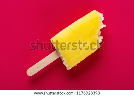yellow popsicle with some bites on a rose red background