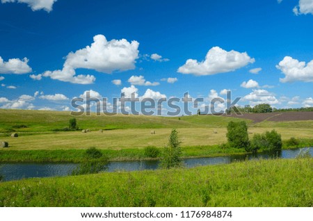 Sunny summer landscape with river,fields,green hills,hay bales and beautiful clouds in blue sky.River Upa in Tula region,Russia. 