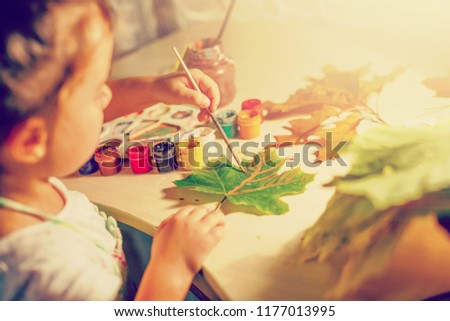 Cute little girl drawing with paint autumn leaves at home