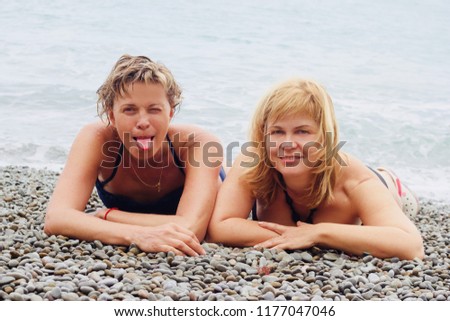 Best friends/ Two nice middle-aged women are lying on the pebble beach near the seashore Royalty-Free Stock Photo #1177047046