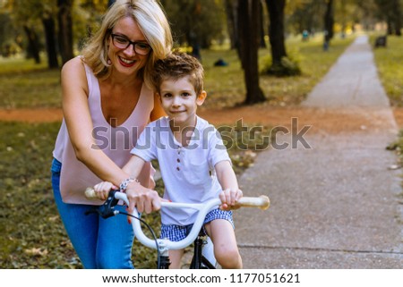 Little boy learning to drive a bike with his mom