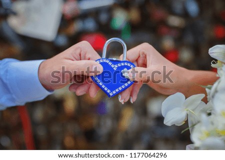 The hands of the newlyweds hold the lock in the shape of a blue heart