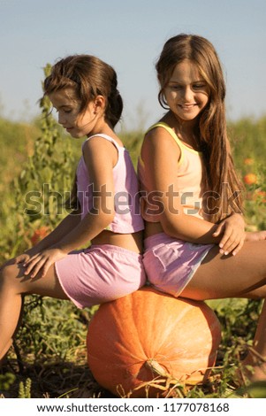 Two girls are sitting on a pumpkin on the field. Halloween