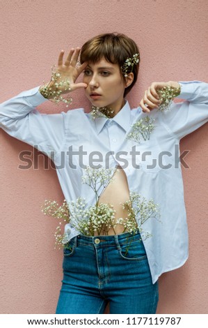 
Portrait of a beautiful girl model with flowers in clothes, which poses on a pink background. Fashionable spring photography. Place for the inscription.