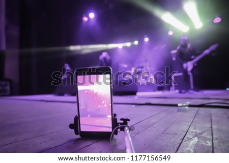 shoot a rock band concert on the phone with a monopod. silhouettes of musicians on stage. to shoot a video on the phone at a concert.