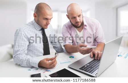 Two serious businessmen using laptop and discussing new project at office, developing strategy for online business, explaining sharing ideas, preparing presentation, having brainstorming session