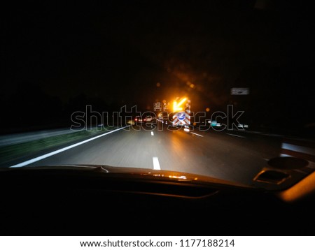 Shot from inside of car driving down road in night time with blurry lights of road signs and security traffic illuminated arrow on truck during accident or road works