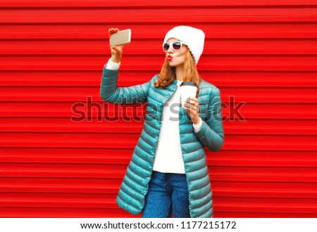 Fashion pretty woman takes a picture self portrait on a smartphone on red background