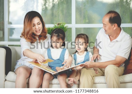 Portrait of asian father mother reading a cartoon book to her daughter at home.