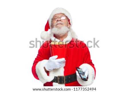 Christmas. Smiling, good Santa Claus in white gloves holding a red bucket of popcorn in one hand, and a TV remote control with his second hand and switches channels. The concept of watching a movie