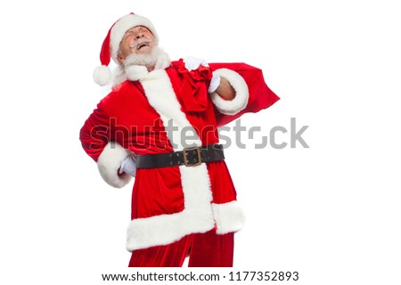 Christmas. Santa Claus is suffering from back pain and holds a red bag with gifts on his back. Isolated on white background.