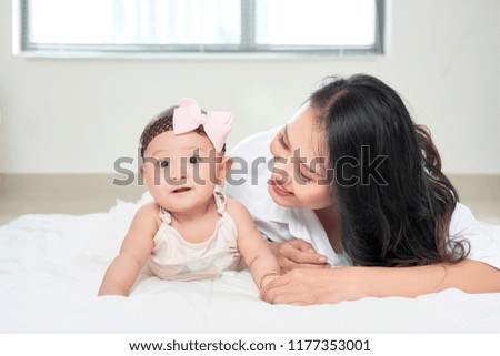 Mother and baby daughter happy and beautiful home together playing on the floor on window background