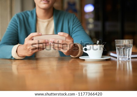 Cropped image of young man drinking coffee in restaurant and checking social media