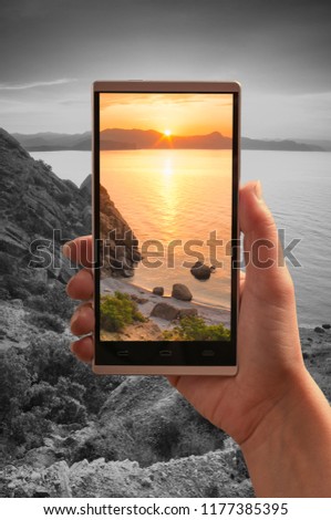 Sunrise over the sea on a screen of smartphone against monochrome background. Travel and adventure concept. 