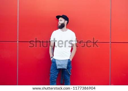 Hipster handsome male model with beard wearing white blank t-shirt and a baseball cap with space for your logo