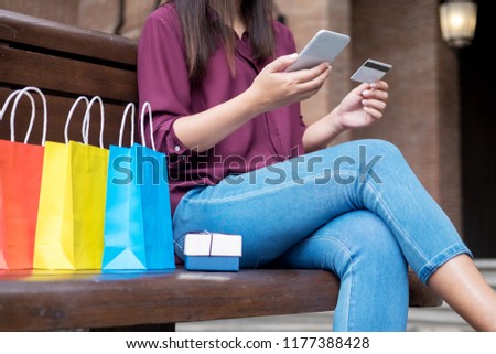 Portrait of a happy shopper paying online with credit card through smartphone with bags in a mall