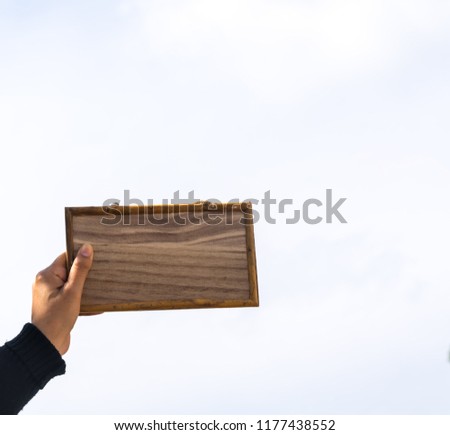 Wooden   picture  frame  in  hand  of
a  woman with   blue  sky   background