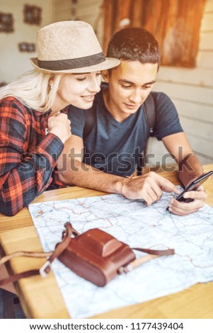 Traveling casual woman and man sitting at table with map and photo camera while using phone