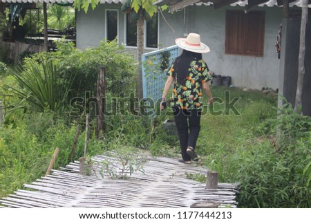 Thai middle-aged woman White with long black hair. Wear a flower pattern and leaves. She sits in a cottage with green fields as the background.  (September) Northern Thailand