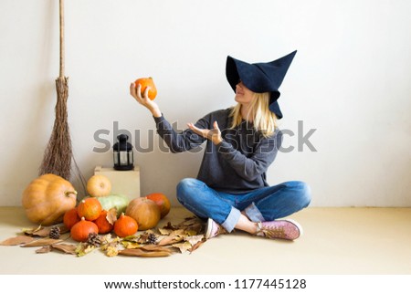Halloween concept. Beautiful blonde girl in a witch hat with pumpkins and a broom on a white background