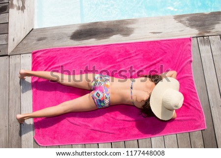 pretty fit young woman lying on towel pink in swimsuit at pool wood deck