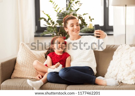 christmas, technology and family concept - happy mother and little daughter taking selfie by smartphone at home