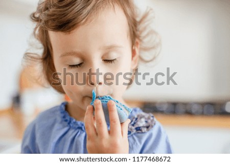 Adorable little girl eating blue macaroons on the white modern kitchen at home