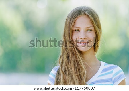 Beautiful smiling teenage girl in blue blouse, against green of summer park.