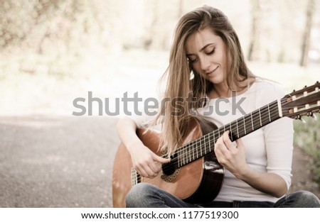 Beautiful young girl with long hair plays guitar in the park. Vintage pic with copy space.