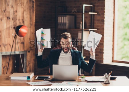 Elegant glad cheerful stylish smart clever bearded handsome attractive business shark, ceo, leader in black jacket, sitting in front of laptop, raising papers with charts at workplace, workstation