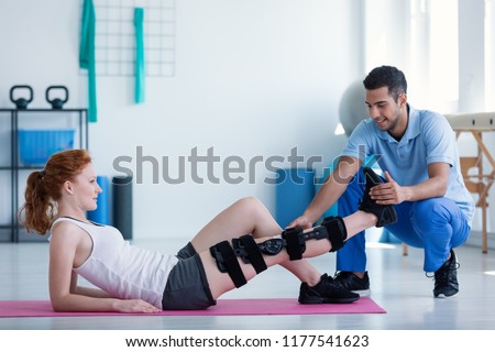 Woman with leg injury on mat and smiling doctor during treatment in the hospital Royalty-Free Stock Photo #1177541623