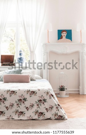 Bed with rose decorated cover and an ornamented fireplace mantel in a high ceiling vintage bedroom interior. Real photo.
