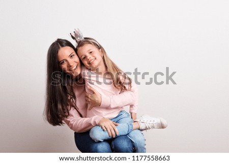 A small girl with crown headband and her mother sitting in a studio.