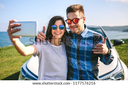 Young couple doing a selfie leaning on the car near the coast