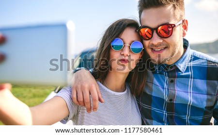 Young couple doing a selfie leaning on the car near the coast
