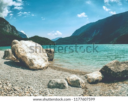 Stones stack on shore of blue green water of mountain lake. Blue mountains in water level mirror.