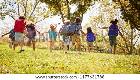 Group of schoolchildren running in a field, back view Royalty-Free Stock Photo #1177631788