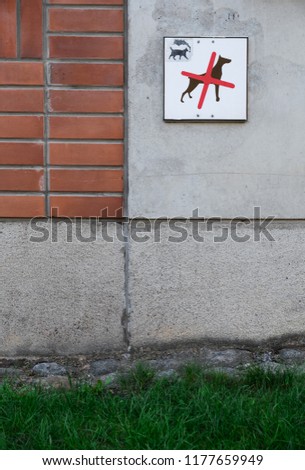No dogs sign with a little smoking cat picture in it on a mixed concrete brick wall and grass at the bottom.