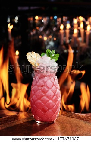 beautiful serve of a pink cocktail with crash, decorated with mint and pineapple slice on copper plates against the background on the real fire. close up.