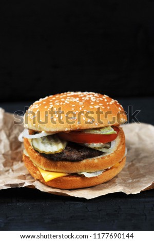 fast food-cut in half or bitten Burger with cheese and beef on Kraft paper on black charcoal background
