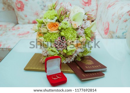 Wedding ring. Two gold diamond rings of the bride and groom are in a red box near the bride's bouquet of delicate flowers and passports of the Russian Federation