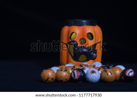 Pumpkin shaped halloween lantern with black cat coming out With lots of round chocolate sweets enclosed in a funny face, on a black background. Useful to represent a funny event for halloween