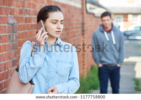 Woman Calling For Help On Mobile Phone Whilst Being Stalked On City Street By Man Royalty-Free Stock Photo #1177718800