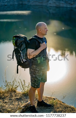 a traveler with a backpack examines the territory around the river on a sunny day. The tourist is embraced by the beauty of nature