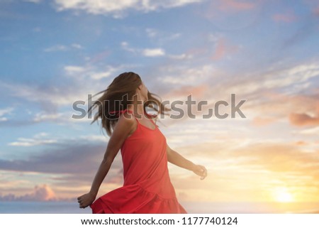 Beautiful young woman in a red dress is enjoying the good weather and the nice view of the sea and the mountains